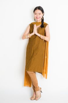 Portrait of mixed race Indian Chinese girl in traditional punjabi dress greeting, full length standing on plain white background.