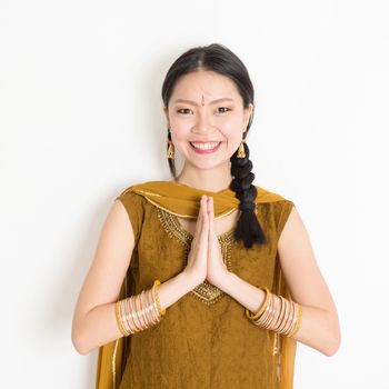 Portrait of young mixed race Indian Chinese girl in traditional punjabi dress with greeting pose, standing on plain white background.