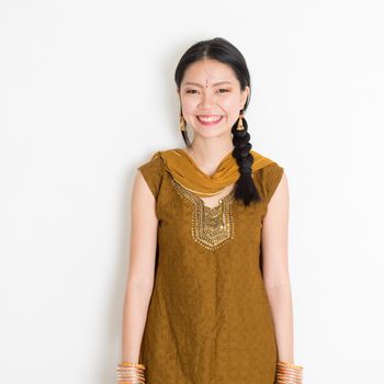 Portrait of young mixed race Indian Chinese female in traditional Punjabi dress smiling, standing on plain white background.