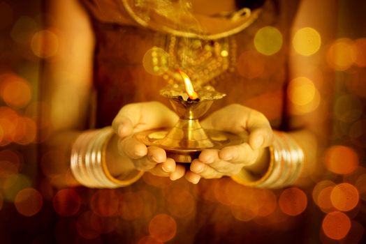 Close up Indian woman in traditional dress hands holding diya oil lamp and celebrating Diwali or deepavali, fesitval of lights.