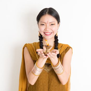 Mixed race Indian Chinese female in traditional dress hands holding diya oil lamp and celebrating Diwali or deepavali, fesitval of lights.
