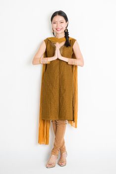 Portrait of mixed race Indian Chinese woman in traditional punjabi dress greeting, full length standing on plain white background.