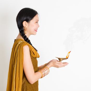 Side view young mixed race Indian Chinese woman in traditional dress hands holding diya oil lamp and celebrating Diwali or deepavali, fesitval of lights.