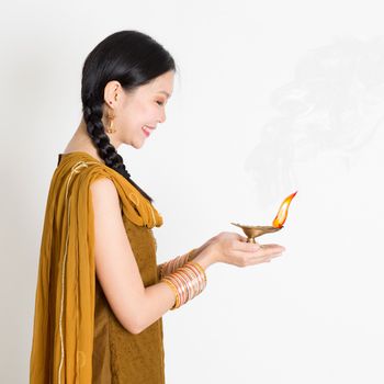 Profile view young mixed race Indian Chinese female in traditional dress hands holding diya oil lamp and celebrating Diwali or deepavali, fesitval of lights.