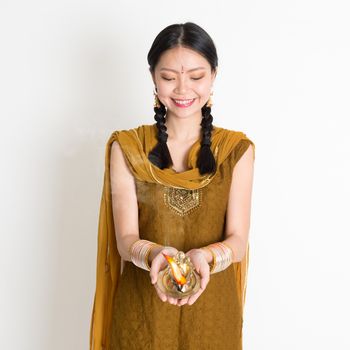 Young mixed race Indian Chinese woman in traditional dress hands holding diya oil lamp and celebrating Diwali or deepavali, fesitval of lights.