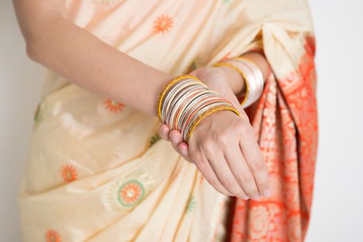 Fair skin Indian woman in traditional sari dress wearing bangles, standing on plain background.