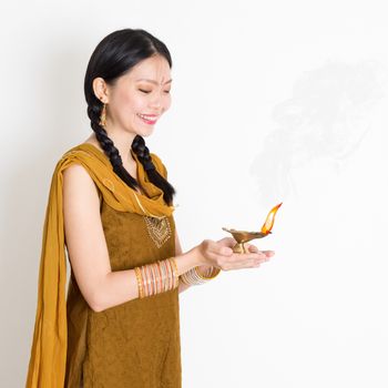 Young mixed race Indian Chinese female in traditional dress hands holding diya oil lamp and celebrating Diwali or deepavali, fesitval of lights.