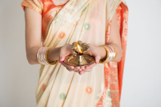 Indian girl in traditional sari dress, holding diwali oil lamp diya, on plain background.