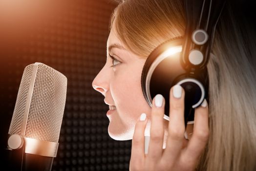 Female Voice Talent in Recording Studio. Girl Recording Voice Over For Radio Commercial. Young Girl in Her 20s and the Shiny Metallic Pro Microphone.