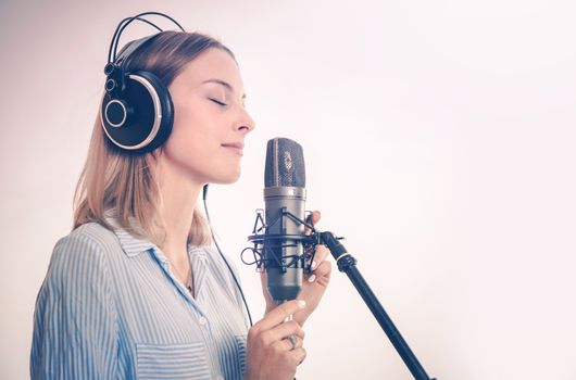 Female Vocal Recording. Young Woman with Microphone and Headphones in the Recording Studio.