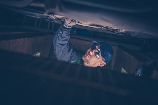 Professional Caucasian Car Mechanic Fixing Broken Elements Under the Car.