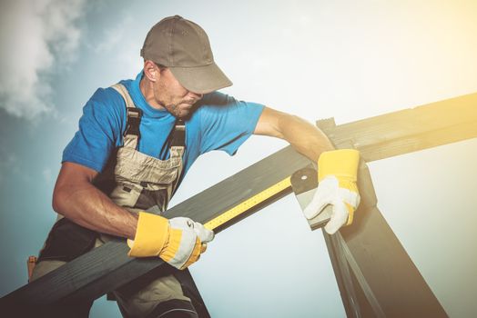 Wood Construction Job. Caucasian Construction Worker Measuring Wood Elements.