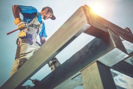 Wood Construction Works. Caucasian Worker on the Wooden Roof Construction.