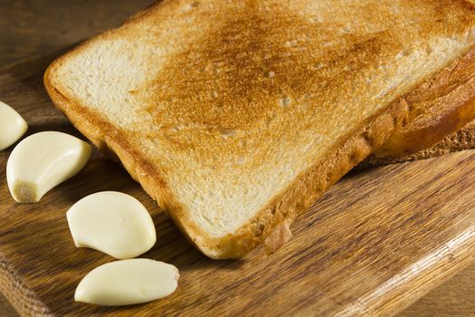 Fried bread and cloves of fresh garlic on a wooden cutting board