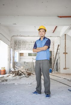 Asian construction worker with hardhat standing at site. 