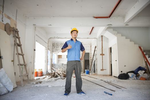 Asian construction worker with hardhat giving a thumb up at site, house renewal concept.