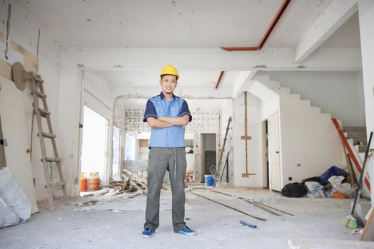 Asian construction worker with hardhat standing at site, house improvement concept.