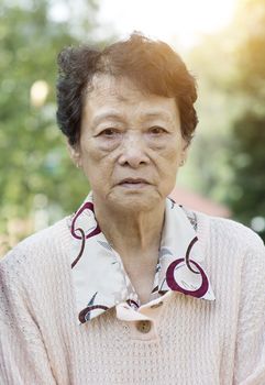 Portrait of upset Asian senior adult woman at outdoor garden park in the morning.