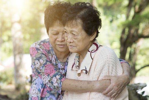 Candid shot of Asian elderly woman consoling her friend at outdoor park in the morning.