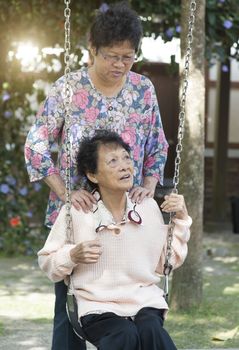 Portrait of Asian elderly women playing swing at outdoor playground, morning in the park.