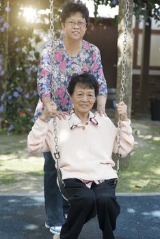 Portrait of Asian old women playing swing at outdoor playground, morning in the park.