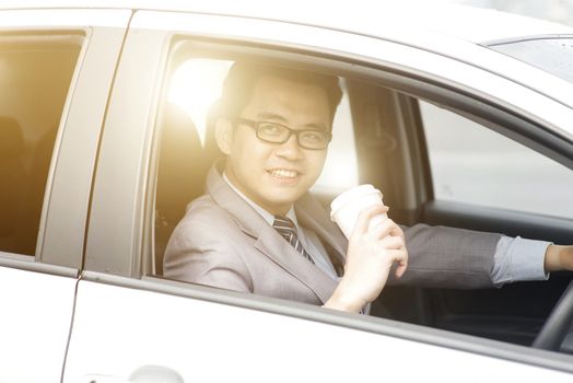 Asian business man driving a car and holding paper cup of coffee in morning with beautiful sunlight.