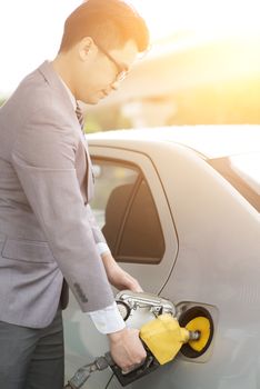 Refueling gas. Asian business man hand holding nozzle and pumping gasoline fuel in car at petrol station.