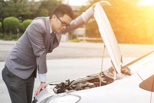 Young Asian business man looking under the hood of breakdown car.
