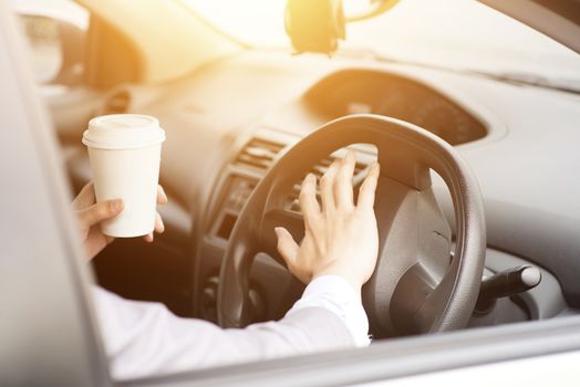 Concept photo of close up hand on steering honking while driving in morning, another hand holding coffee cup.