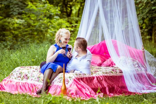 Man and woman sitting on the bed in the lawn and holding a glasses of wine and look at each other in Lviv, Ukraine.