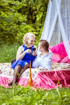 Man and woman sitting on the bed in the lawn and holding a glasses of wine and look at each other in Lviv, Ukraine.