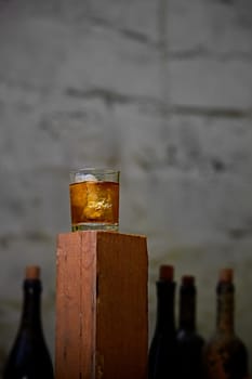 A glass of whiskey with ice on old wooden bar around the old bottles. Shallow dof