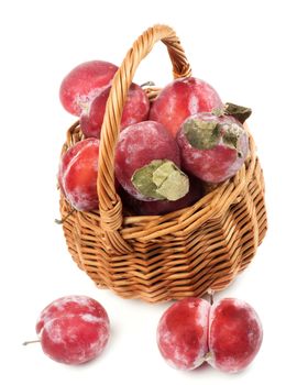 Delicious Fresh Frozen Red Plums with Leafs in Wicker Basket isolated on White background