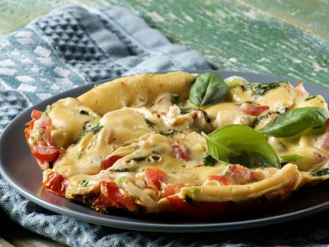 Fluffy Omelet with Vegetables, Greens and Basil Leafs on Grey Plate and Blue Napkin. Focus on Foreground