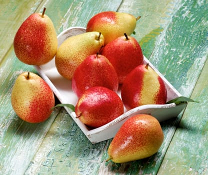 Heap of Ripe Yellow and Red Pears with Leafs in White Wooden Tray closeup on Cracked Wooden background