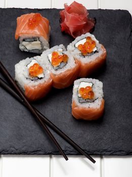 Delicious Sushi with Smoked Sliced Salmon and Gourmet Red Caviar and Ginger on Stone Plate with Chopsticks with Shadows closeup on White Plank background