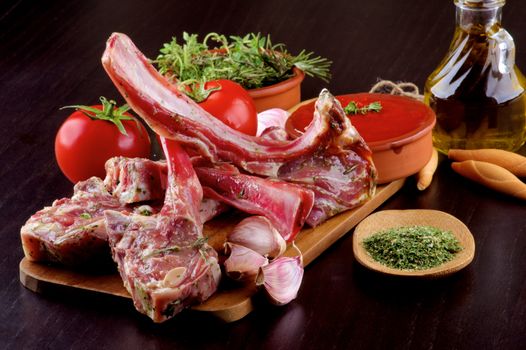 Arrangement of Raw Lamb Ribs with Tomatoes, Spices, Olive Oil and Garlic on Wooden Cutting Board closeup on Dark Wooden background
