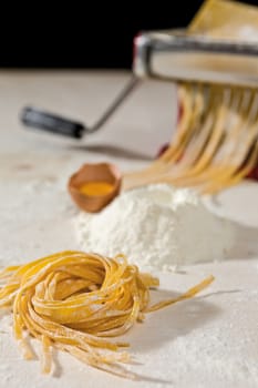 Tagliatelle pasta and its ingredients with machine pasta cutter on background