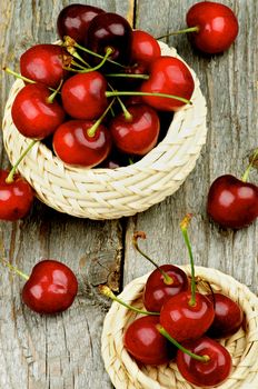 Ripe Red Sweet Cherries with Stems in Wicker Bowls closeup on Rustic Wooden background. Top View