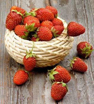Arrangement of Fresh Ripe Forest Strawberries in Wicker Bowl closeup on Rustic Wooden background
