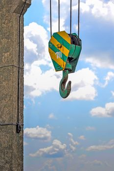 Yellow-green hook of a construction crane hanging on a rope on a background of clouds on a lake dam