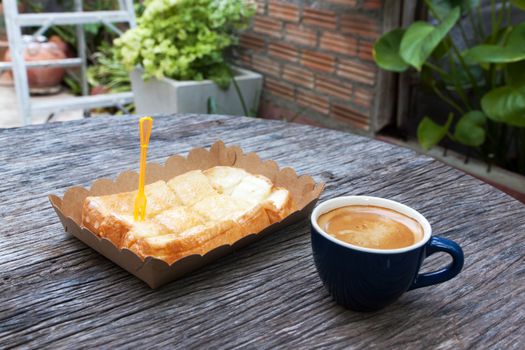 Toast with butter milk in paper tray and espresso on wood table