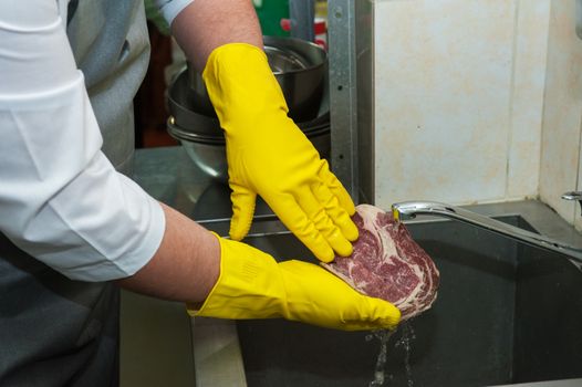 Hands in gloves washing and cleaning meat at the kitchen sink