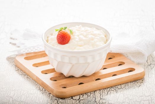 Bowl of creamy rice pudding garnished with a ripe whole strawberry.