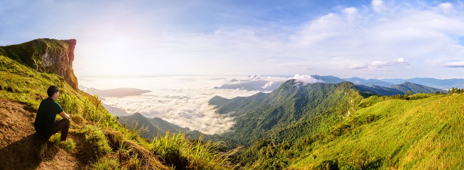 Panorama beautiful landscape nature, Male tourist are watching the sunrise on peak mountain with sun cloud fog and bright sky in winter at Phu Chi Fa Forest Park, famous attraction of Chiang Rai Province, Thailand