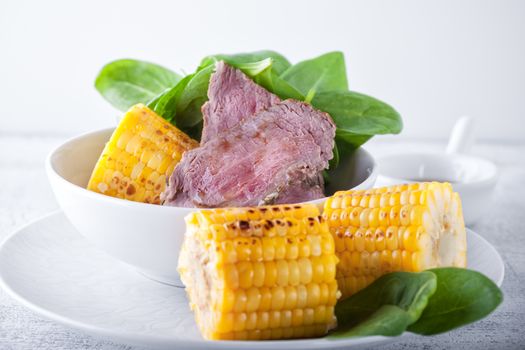 Beef and grilled corn with greenery on a white plate
