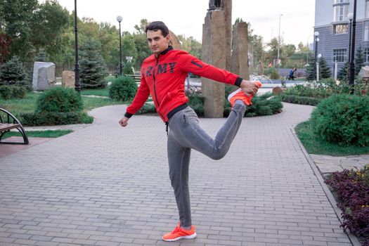 Young fitness man stretches preparing for training workout outdoor