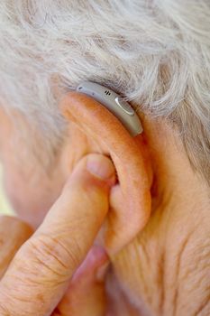 closeup senior woman inserting hearing aid in her ears