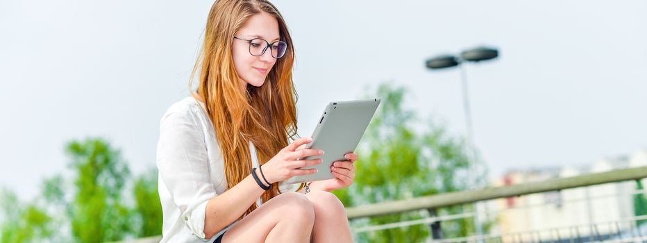 panoramic view on dynamic young executive girl working outside n a touchscreen tablet. Free of any constraint. Symbol of a job search or trade of outsourcing