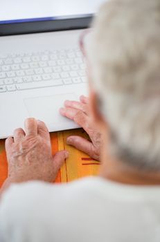 Closeup on pair of old hands typing on a laptop ontop of a desk.